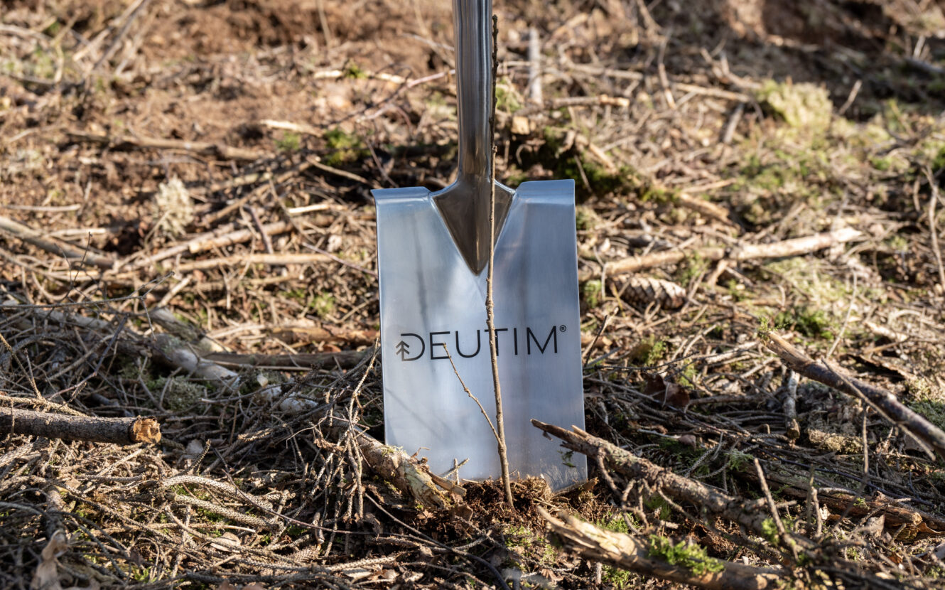 Detailaufnahme eines Edelstahl-Spatens mit DEUTIM Logo, welcher im Waldboden steckt